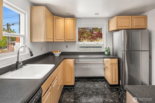 kitchen featuring light brown cabinetry, dark countertops, freestanding refrigerator, and a sink