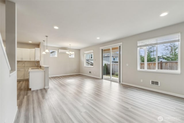 unfurnished living room featuring visible vents, an AC wall unit, light wood-style flooring, a sink, and an inviting chandelier