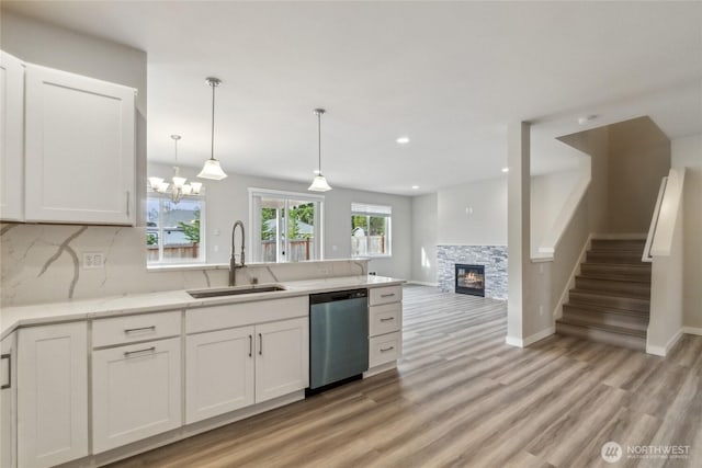 kitchen with a sink, stainless steel dishwasher, white cabinetry, a peninsula, and a stone fireplace