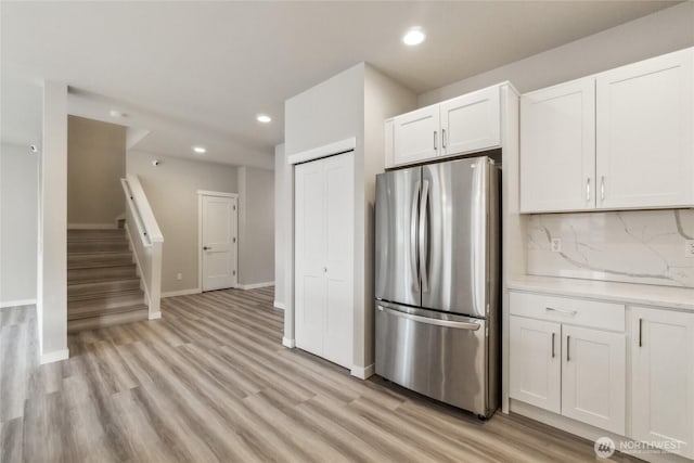 kitchen featuring freestanding refrigerator, white cabinets, light wood finished floors, decorative backsplash, and baseboards