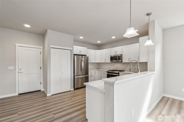 kitchen featuring light wood-style floors, appliances with stainless steel finishes, a peninsula, and light countertops