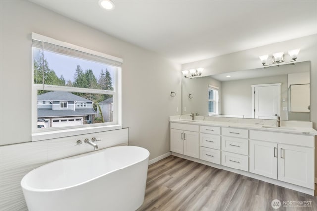 full bathroom featuring a chandelier, a freestanding bath, double vanity, a wealth of natural light, and a sink