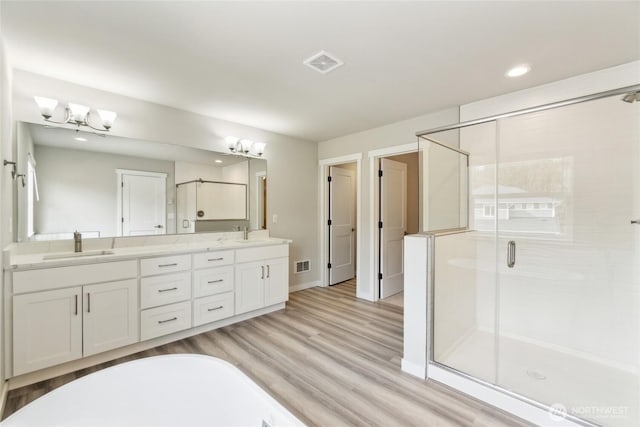 full bath with visible vents, double vanity, a stall shower, wood finished floors, and a sink