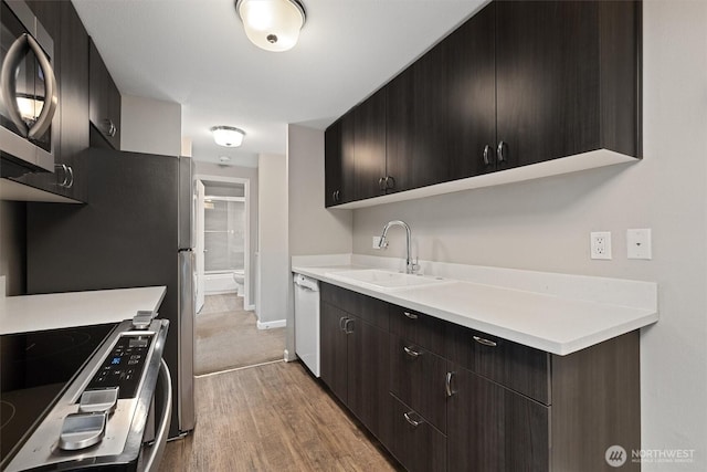 kitchen with white dishwasher, range with electric cooktop, a sink, light wood-style floors, and stainless steel microwave