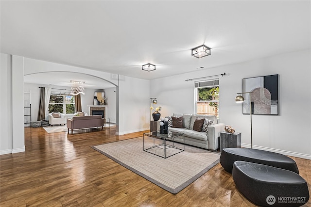 living area with arched walkways, a fireplace, baseboards, and wood finished floors