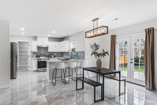 kitchen with marble finish floor, under cabinet range hood, french doors, appliances with stainless steel finishes, and a peninsula