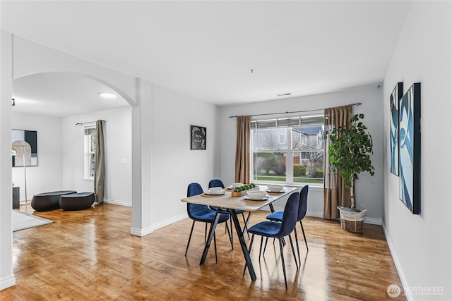 dining area featuring baseboards, arched walkways, and light wood-style floors