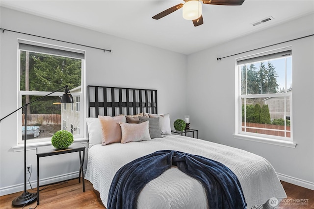 bedroom featuring a ceiling fan, wood finished floors, visible vents, and baseboards