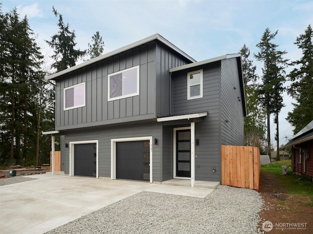 view of front of house with an attached garage, board and batten siding, driveway, and fence