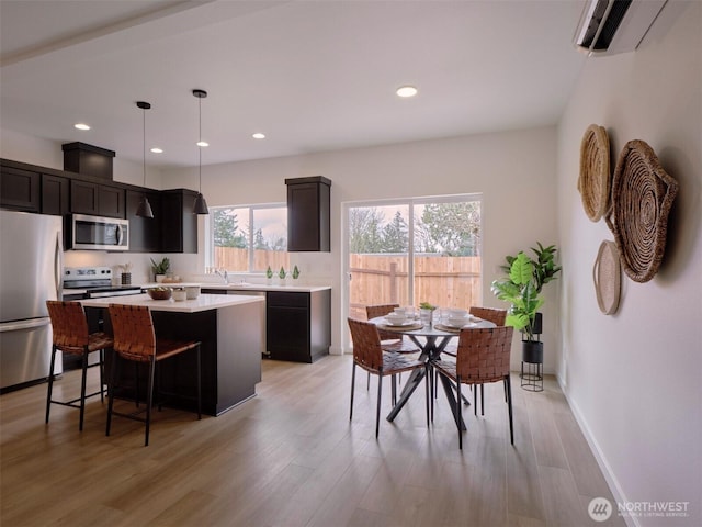 kitchen with light wood-type flooring, a wall mounted AC, a center island, appliances with stainless steel finishes, and light countertops