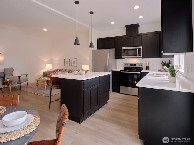 kitchen featuring light wood finished floors, open floor plan, a kitchen bar, light countertops, and stainless steel appliances