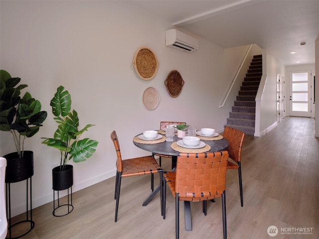 dining area with stairway, light wood-type flooring, a wall mounted AC, and baseboards