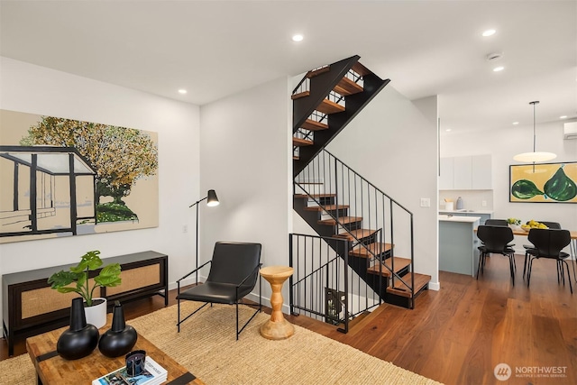 sitting room with recessed lighting, stairway, wood finished floors, and a wall unit AC