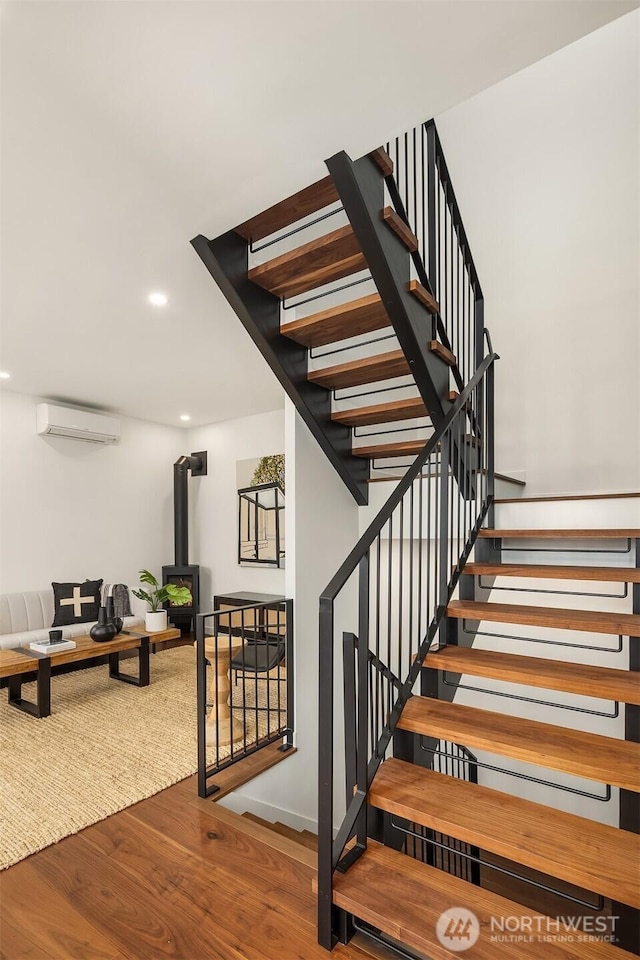 staircase featuring recessed lighting, wood finished floors, a wood stove, and a wall mounted AC