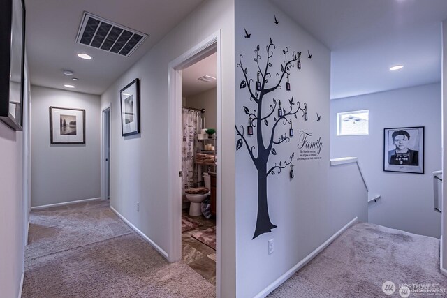 hallway featuring an upstairs landing, visible vents, baseboards, and carpet