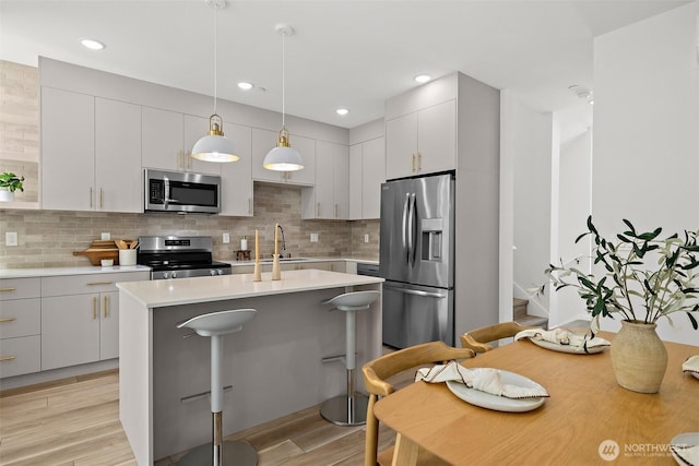 kitchen with a kitchen island with sink, a sink, stainless steel appliances, light wood finished floors, and light countertops