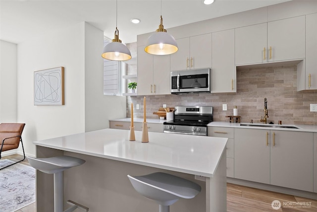 kitchen featuring a breakfast bar area, a sink, decorative backsplash, light countertops, and stainless steel appliances