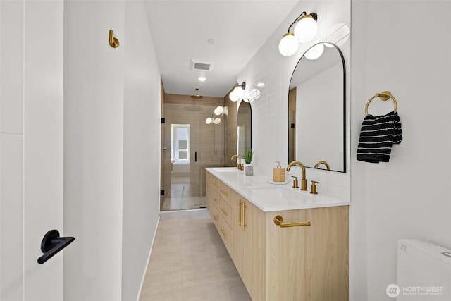 full bath with a sink, visible vents, tiled shower, and double vanity