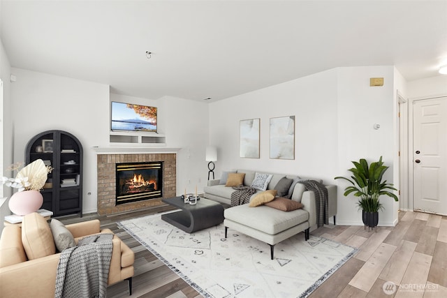 living area featuring light wood-style flooring, a brick fireplace, and baseboards