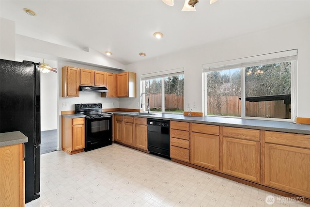 kitchen featuring under cabinet range hood, light floors, black appliances, and a sink