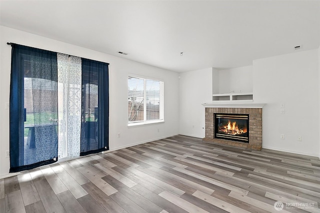 unfurnished living room featuring visible vents, a fireplace, baseboards, and wood finished floors