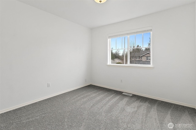 spare room with dark colored carpet, visible vents, and baseboards