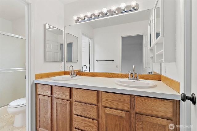 full bathroom with a sink, a shower with shower door, toilet, and double vanity