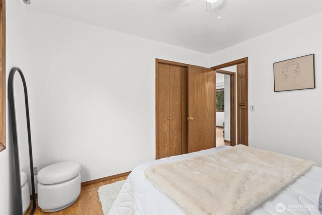 bedroom with a closet, baseboards, wood finished floors, and a ceiling fan