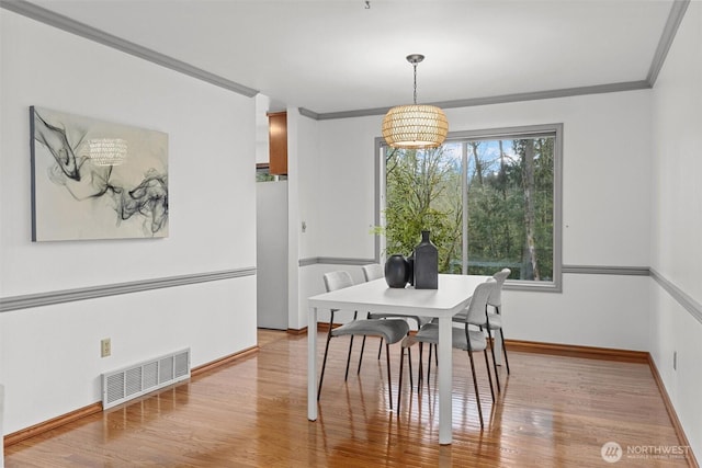 dining room featuring visible vents, wood finished floors, baseboards, and ornamental molding