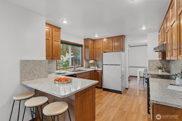 kitchen featuring brown cabinets, a sink, freestanding refrigerator, ventilation hood, and a peninsula