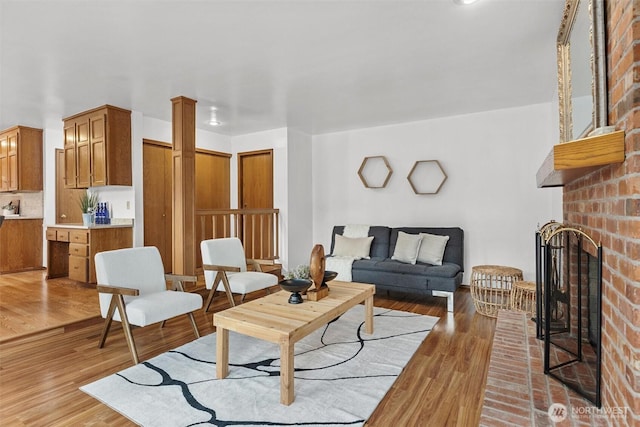 living area featuring a fireplace, light wood-style floors, and ornate columns