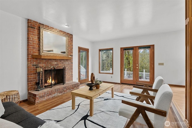 living room featuring a brick fireplace, light wood-style floors, baseboards, and french doors