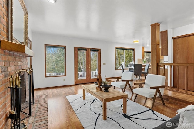 living room featuring french doors, baseboards, light wood-style floors, and a brick fireplace