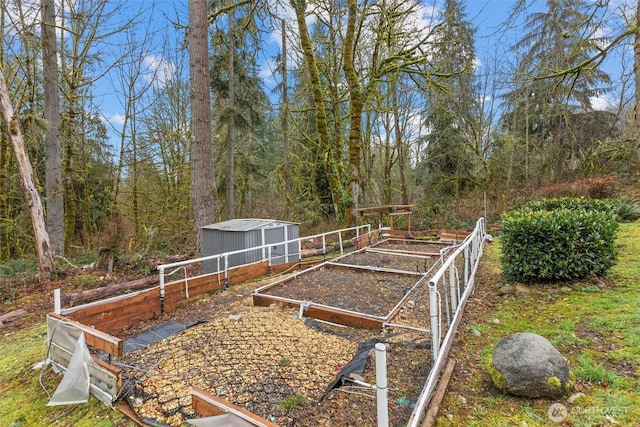 view of yard featuring an outdoor structure, a garden, fence, and a wooded view