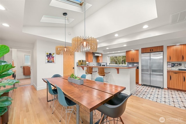 dining space featuring light wood-type flooring, visible vents, lofted ceiling with skylight, recessed lighting, and baseboards