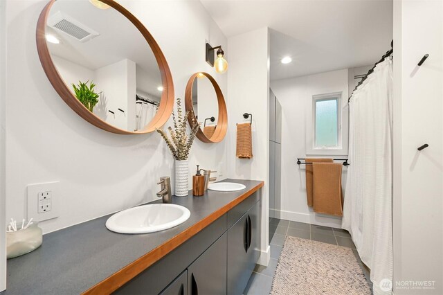 bathroom featuring tile patterned floors, visible vents, double vanity, and a sink