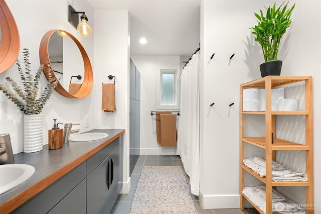 full bath featuring tile patterned floors, double vanity, baseboards, and a sink