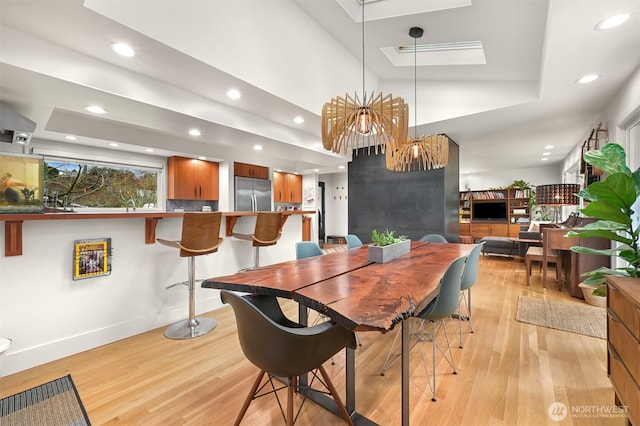 dining room featuring a tray ceiling, light wood-type flooring, a skylight, and recessed lighting