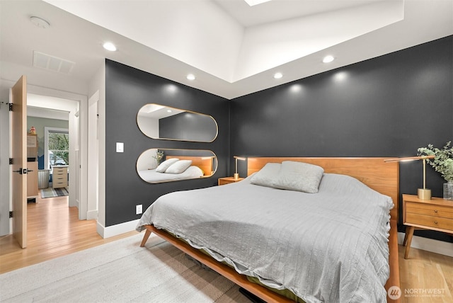 bedroom with an accent wall, a skylight, baseboards, and light wood-type flooring