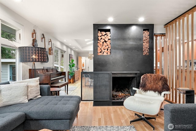 living room featuring plenty of natural light, recessed lighting, a warm lit fireplace, and wood finished floors