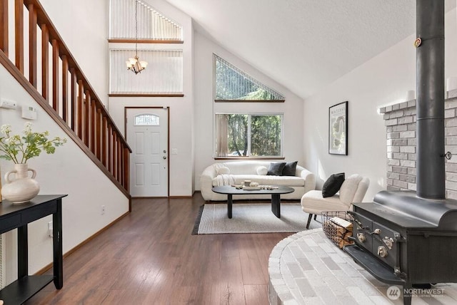 foyer featuring wood finished floors, high vaulted ceiling, an inviting chandelier, a wood stove, and stairs