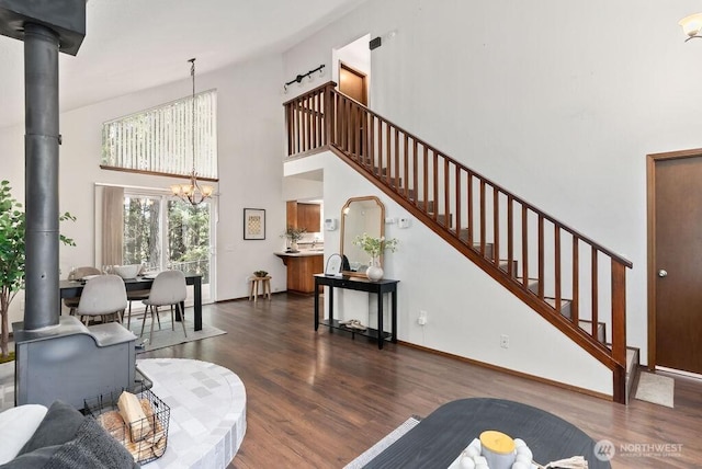 living room featuring baseboards, stairs, a wood stove, an inviting chandelier, and wood finished floors