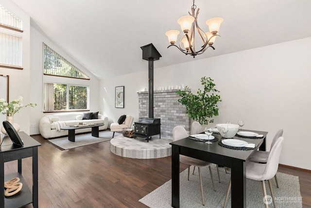 dining space featuring a notable chandelier, high vaulted ceiling, wood finished floors, baseboards, and a wood stove