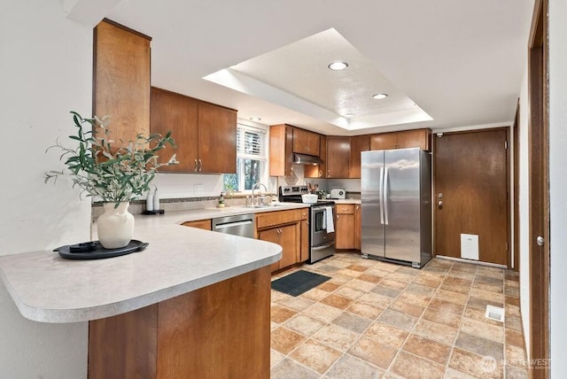 kitchen featuring under cabinet range hood, light countertops, appliances with stainless steel finishes, a raised ceiling, and a sink