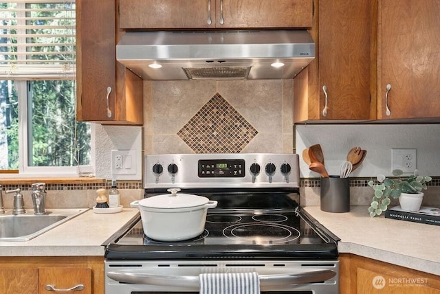 kitchen featuring brown cabinetry, stainless steel range with electric cooktop, extractor fan, and a sink