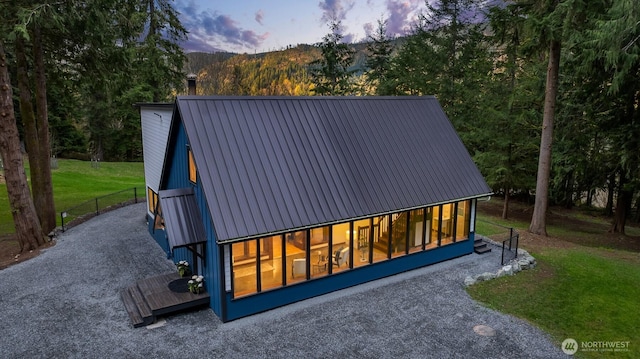 view of front of home with a front lawn, metal roof, gravel driveway, and a wooded view