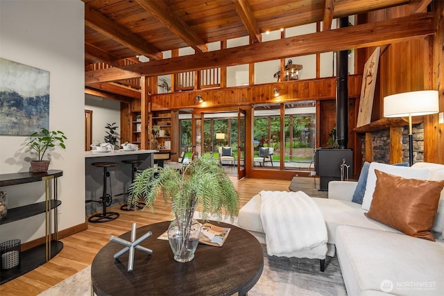 living area featuring beamed ceiling, light wood finished floors, baseboards, a wood stove, and wooden ceiling