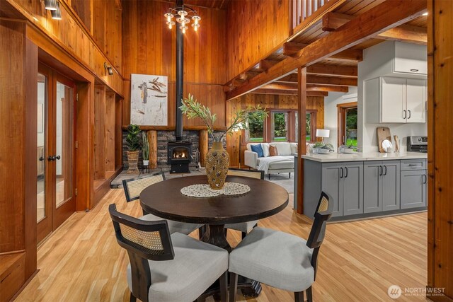 dining space featuring a towering ceiling, wood walls, french doors, and light wood-type flooring
