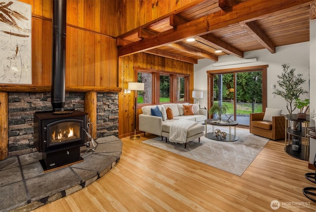 living room with beamed ceiling, wooden walls, wood finished floors, a wood stove, and wooden ceiling
