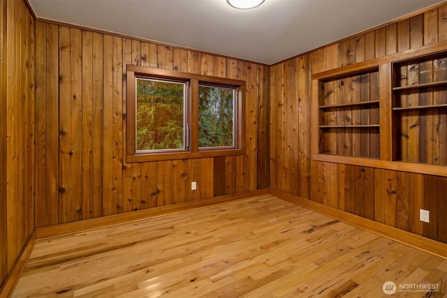 spare room featuring baseboards, wood walls, and wood-type flooring